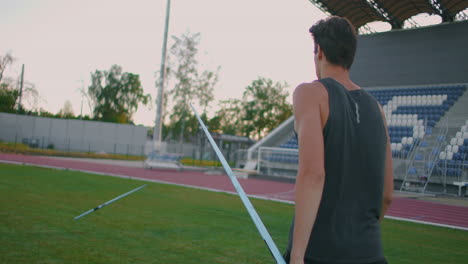 Ein-Speerwerfer-Läuft-Mit-Speeren-Durch-Das-Stadion-Und-Sammelt-Sie-Ein.-Gehen-Sie-Mit-Einem-Speer-In-Der-Hand-Vor-Dem-Hintergrund-Der-Stadiontribüne.-Das-Training-Des-Olympiasiegers.